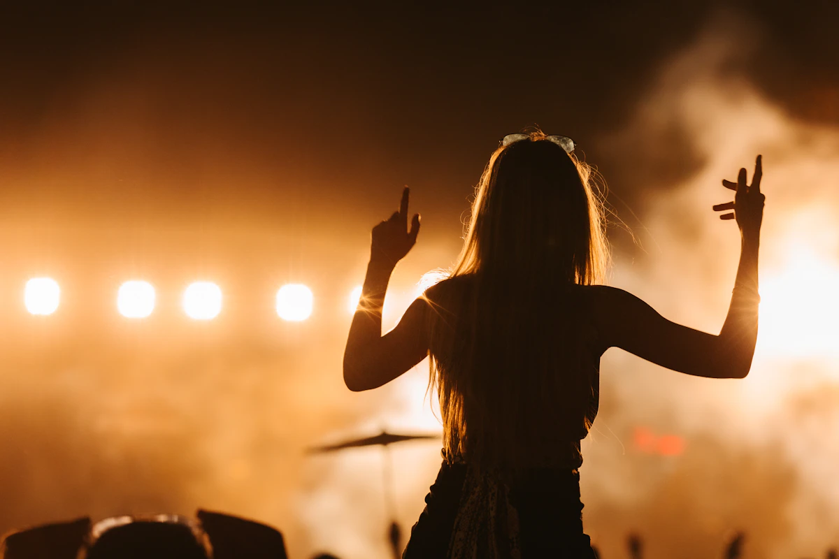 A singer standing before a packed crowd in a dark hall, warm light rising behind her.