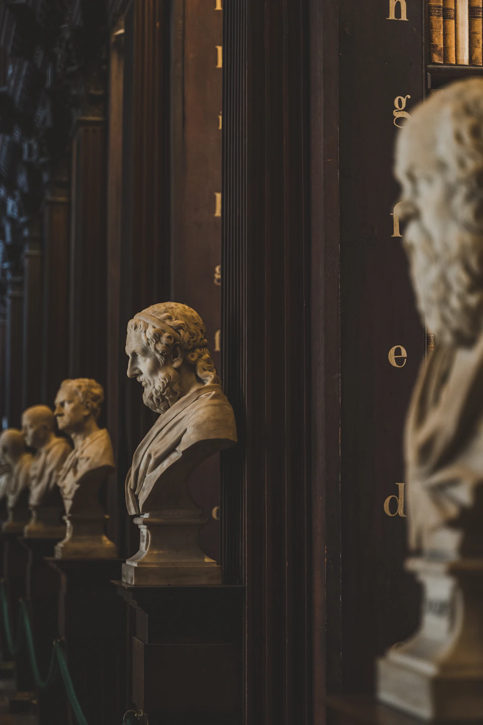 Row of six white stone busts arranged around a dark wooden column