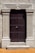 A robust wooden door framed by ornate stone pillars built into a beige stone facade. The door is dark brown and features a series of evenly spaced round metal studs and a central metallic handle.