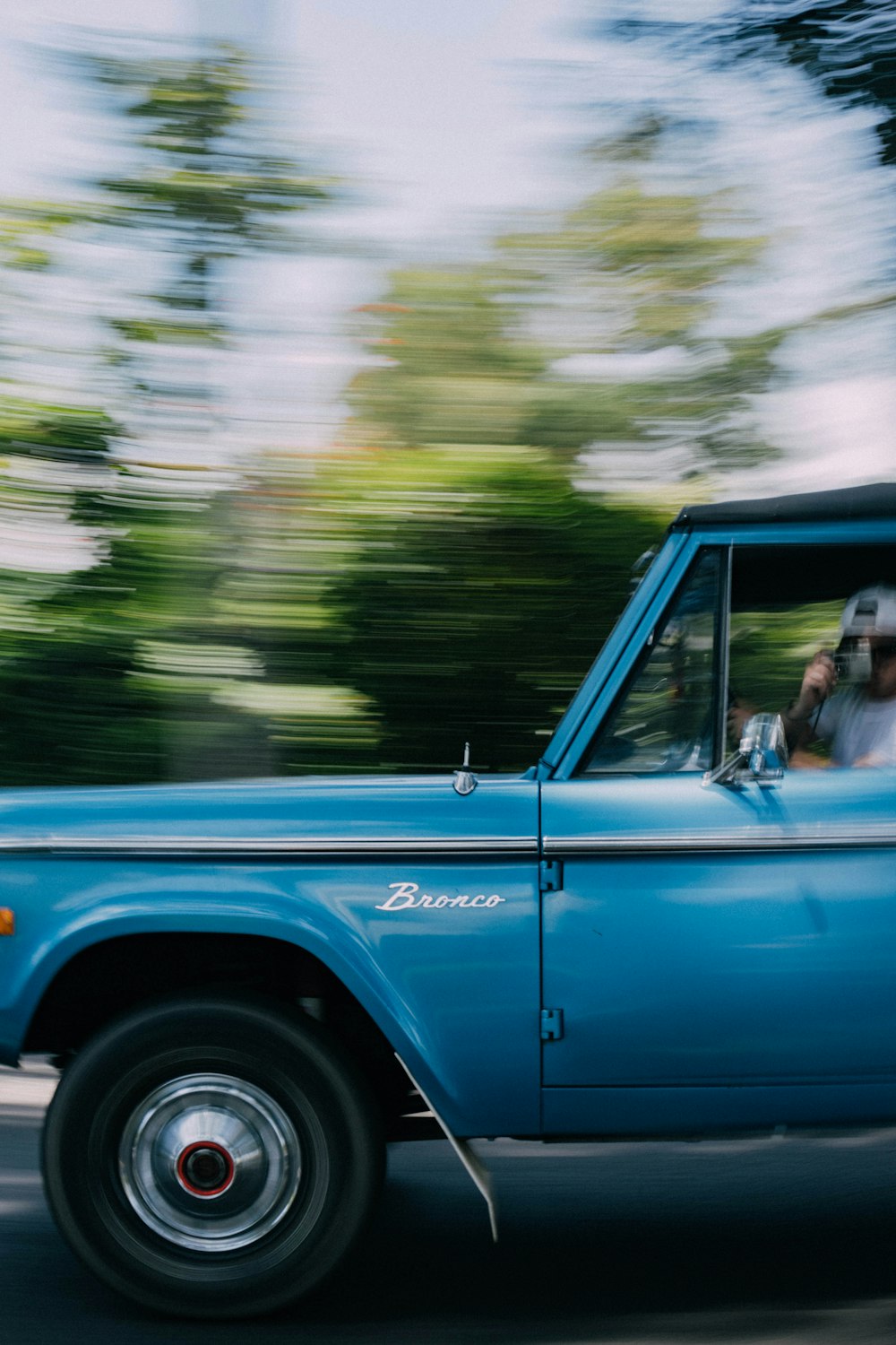 a blue truck driving down a street next to a forest