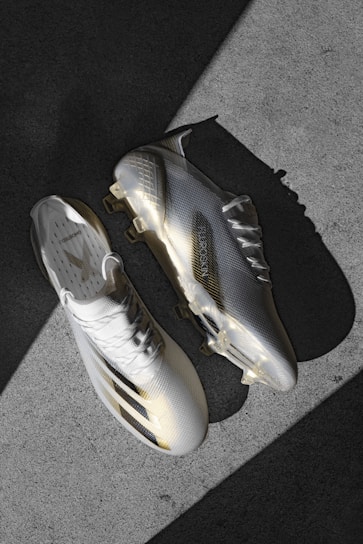 A pair of sleek and modern football cleats are positioned on a textured concrete surface. The shoes have a glossy finish with a combination of white and light gray colors, and feature a subtle pattern. The cleats cast defined shadows, indicating a strong light source from the side.