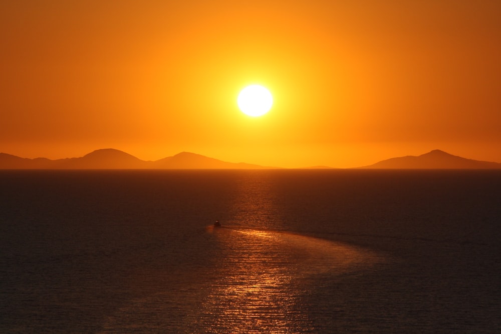 the sun is setting over the ocean with a boat in the water