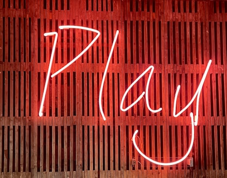 Bright neon sign displaying the word 'Play' with a smiling face, set against a wooden slatted background.