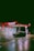 A brightly lit gas station at night with a Texaco sign and a convenience store called StarMart. A dark-colored car is parked near the gas pumps. The ground is wet, reflecting the lights from the station, creating a moody and cinematic atmosphere.