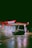 A brightly lit gas station at night with a Texaco sign and a convenience store called StarMart. A dark-colored car is parked near the gas pumps. The ground is wet, reflecting the lights from the station, creating a moody and cinematic atmosphere.