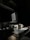 A dimly lit workspace with a computer monitor, keyboard, mouse, and various office items on a desk. A coffee mug is positioned to the right of the keyboard. Natural light from a window casts shadows across the room, highlighting the clean, organized setup.