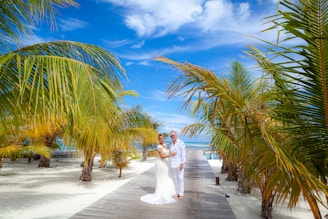 a bride and groom standing on a boardwalk between palm trees