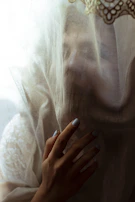 Sophisticated close-up of a hand with deep red nails gently touching a smooth ivory silk fabric.