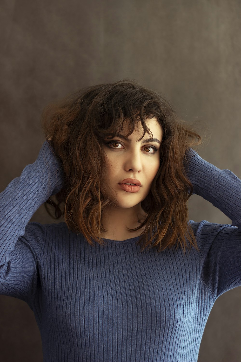 a woman in a blue sweater is holding her hair