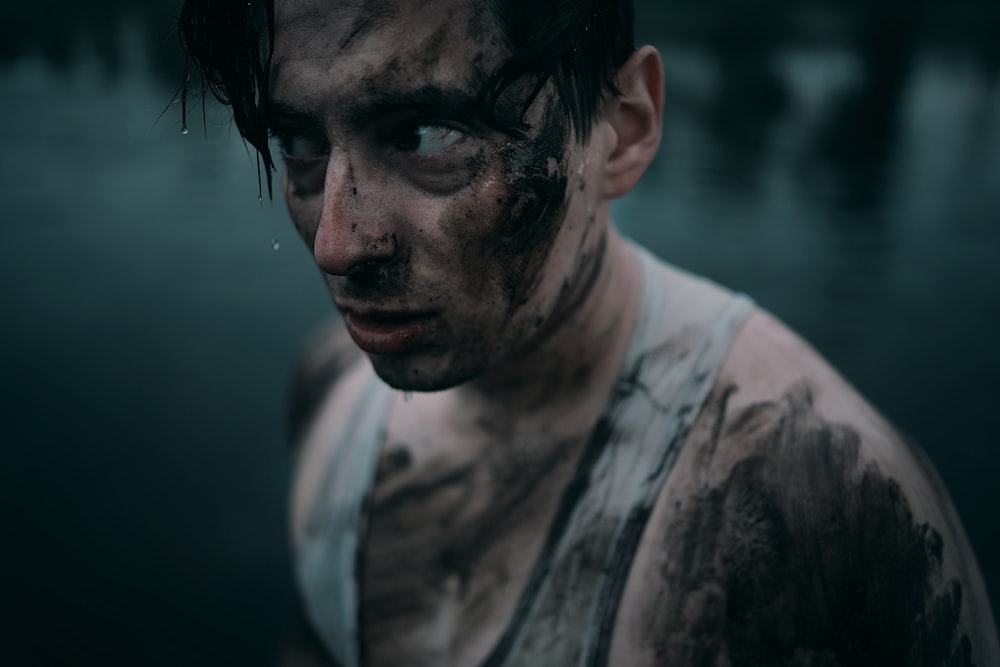 a man covered in mud standing next to a body of water