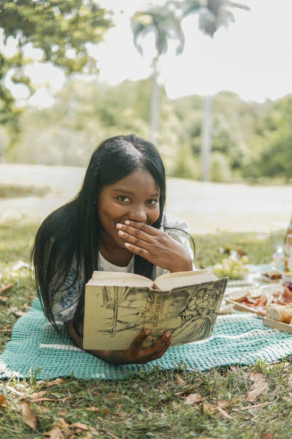 a girl laying on a blanket reading a book