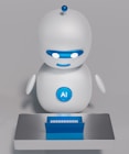 A small, white humanoid robot with blue accents, including eyes, mouth, and a circular badge with the letters 'AI' on its chest, is positioned in front of a blue laptop on a metallic surface. The robot has a simple, smooth design with two cylindrical arms and a small antenna on top.