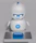 A small, white humanoid robot with blue accents, including eyes, mouth, and a circular badge with the letters 'AI' on its chest, is positioned in front of a blue laptop on a metallic surface. The robot has a simple, smooth design with two cylindrical arms and a small antenna on top.