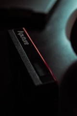 A close-up view of a rectangular electronic device with the brand name 'Aputure' visible on its side. The lighting is dim, creating a dramatic and moody effect. The device appears to have a small digital display and a sleek, modern design.