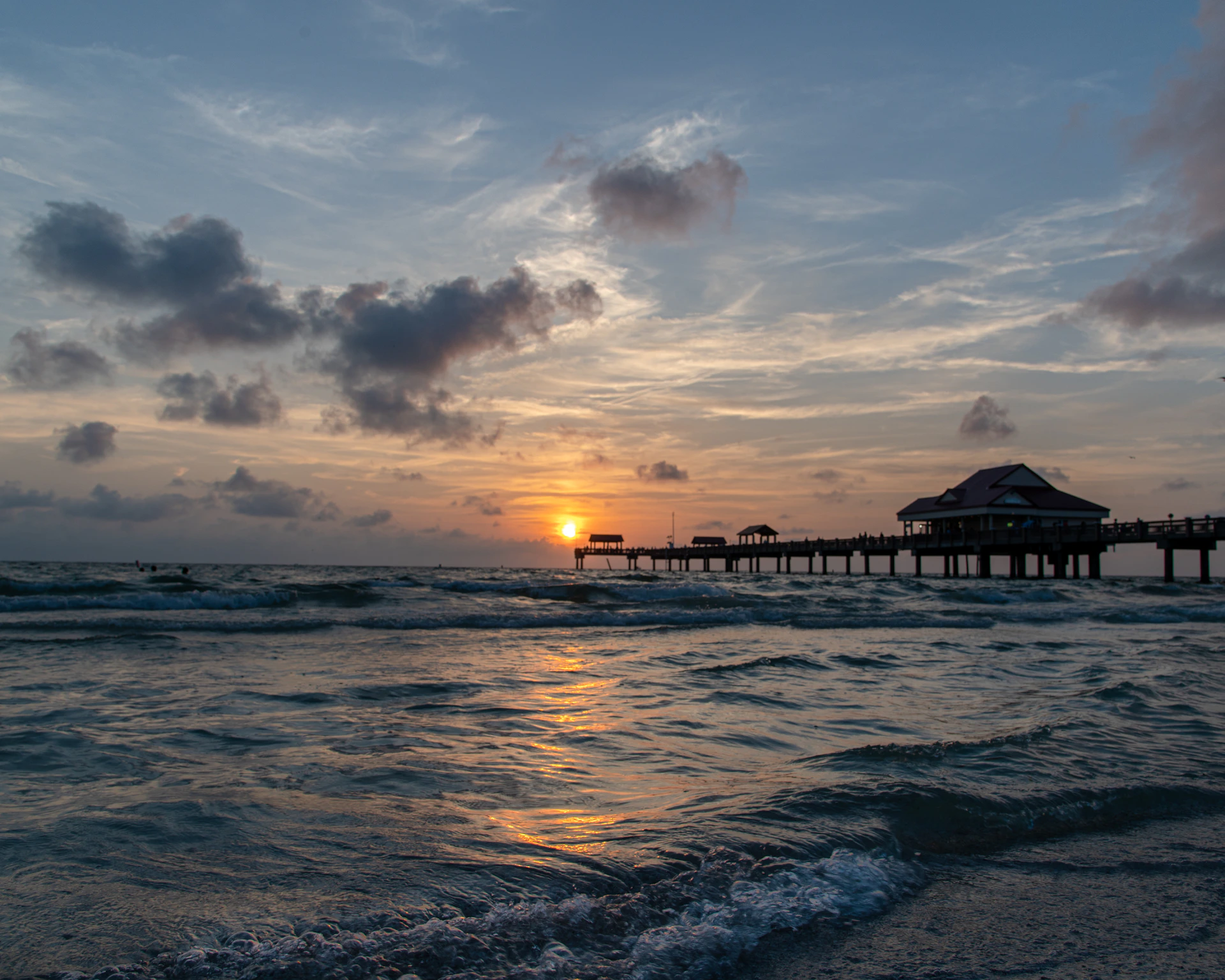 the sun is setting over the ocean with a pier in the background