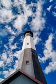 A lighthouse standing tall against a vibrant aqua sky, guiding a nearby cruise ship.