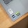 A close-up view of a laptop corner displaying various stickers, including a QR code, Dolby Atmos logo, Intel Evo label, and NVIDIA GeForce RTX badge. The surface is silver, and the laptop is positioned on a wooden desk.
