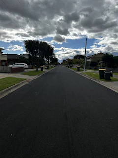 A freshly paved road stretching through a suburban neighborhood under a clear blue sky