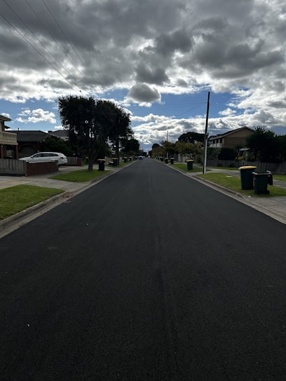 A freshly paved road winding through a suburban neighborhood under a clear blue sky.