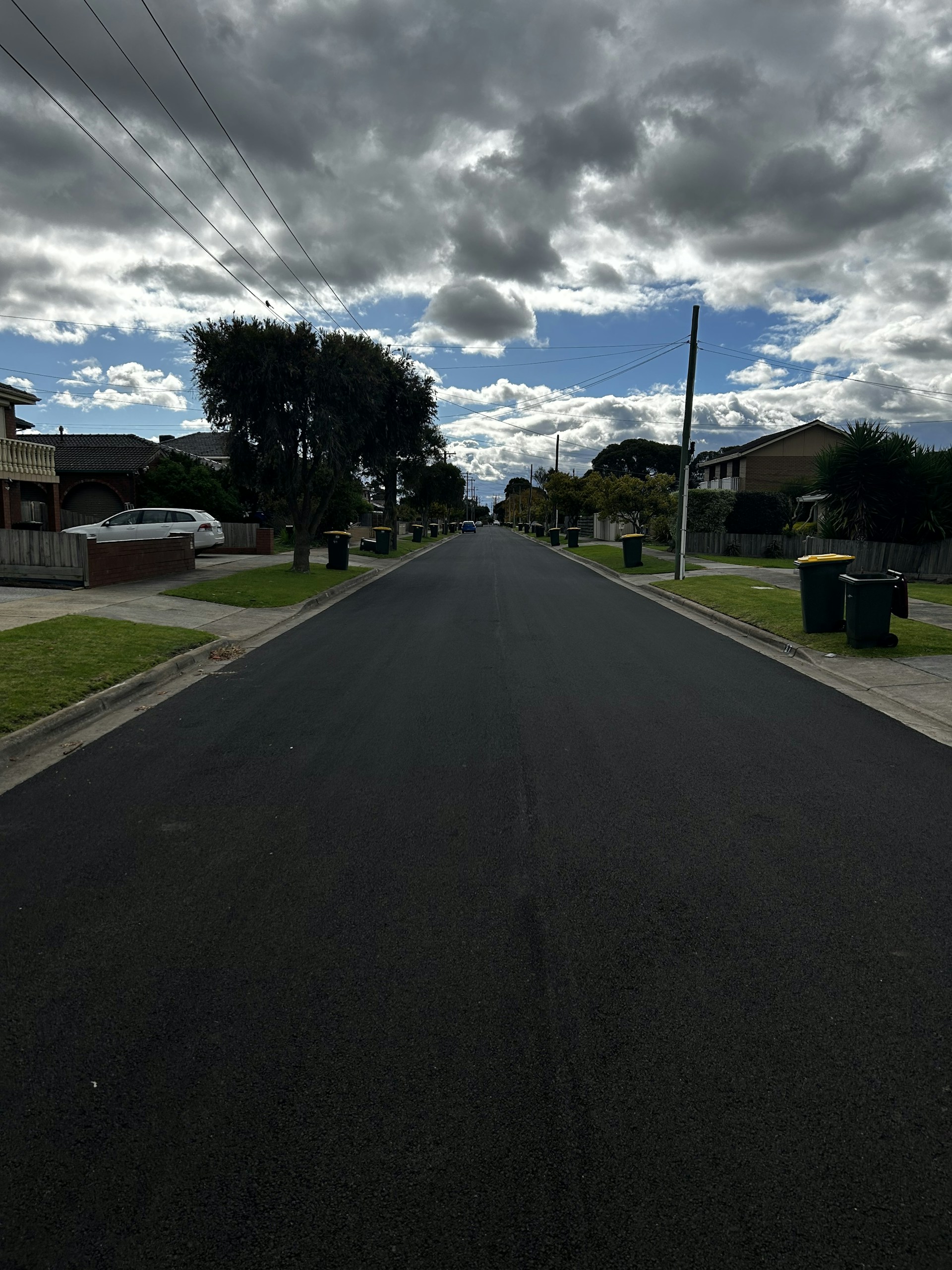 A vibrant, freshly paved road winding through a suburban neighborhood under a bright blue sky.
