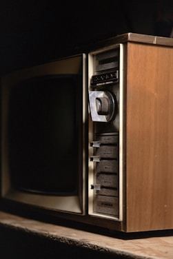 A vintage television set with wood paneling and various manual adjustment knobs and sliders for volume, contrast, brightness, and vertical hold on the side.