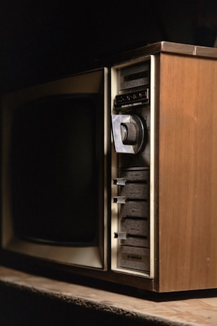 A vintage television set with wood paneling and various manual adjustment knobs and sliders for volume, contrast, brightness, and vertical hold on the side.