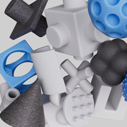 A collection of various 3D geometric shapes, including cubes, spheres, crosses, cones, and cylinders. The textures are rough and the objects are arranged in a seemingly random overlapping fashion. The color palette consists mostly of whites, blues, and blacks.