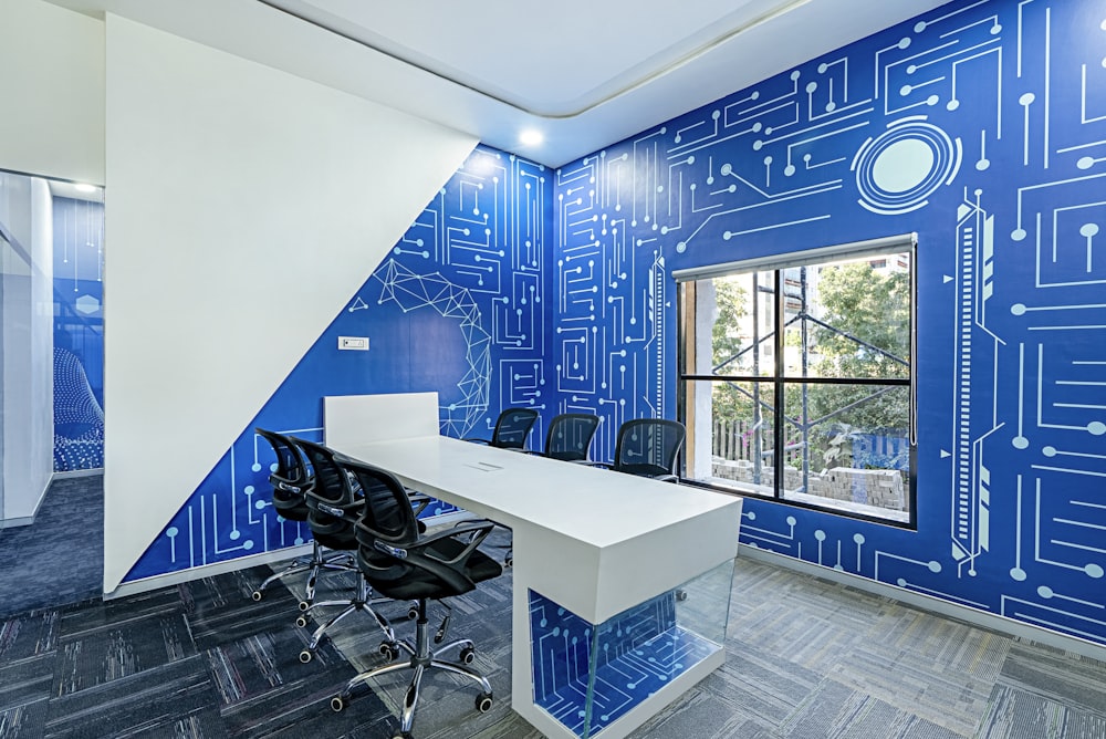 a room with a desk and chairs in front of a blue circuit board wall