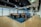 A modern office space with an open-plan layout features workstations separated by colorful dividers. It has a combination of wooden and carpeted flooring, and modern ceiling lighting. The walls are adorned with geometric patterns. An accessible exit sign is visible on the ceiling.
