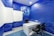 A modern office space features a white desk with two black chairs. The walls are covered with blue wallpaper adorned with digital circuit patterns and a globe, accompanied by a cartoon robot. The room has a futuristic design with a focus on a technological theme.