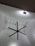 A large black ceiling fan is mounted on a high ceiling with intricate white geometric patterns. Soft lighting creates shadows on the ceiling, enhancing its texture. A series of small string lights are also visible, adding a decorative element.