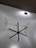 A large black ceiling fan is mounted on a high ceiling with intricate white geometric patterns. Soft lighting creates shadows on the ceiling, enhancing its texture. A series of small string lights are also visible, adding a decorative element.