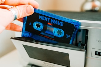 a person holding a blue cassette in front of a metal machine