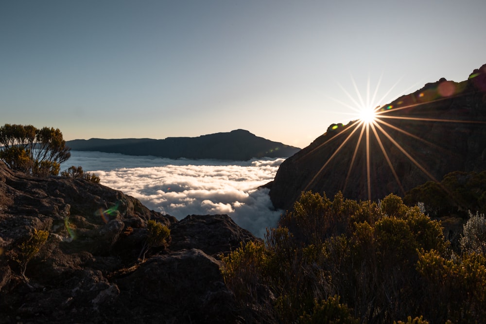 the sun is shining above the clouds in the mountains