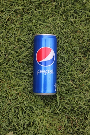 A close-up of a chilled Pepsi can with a straw, resting on a bed of fresh green grass.