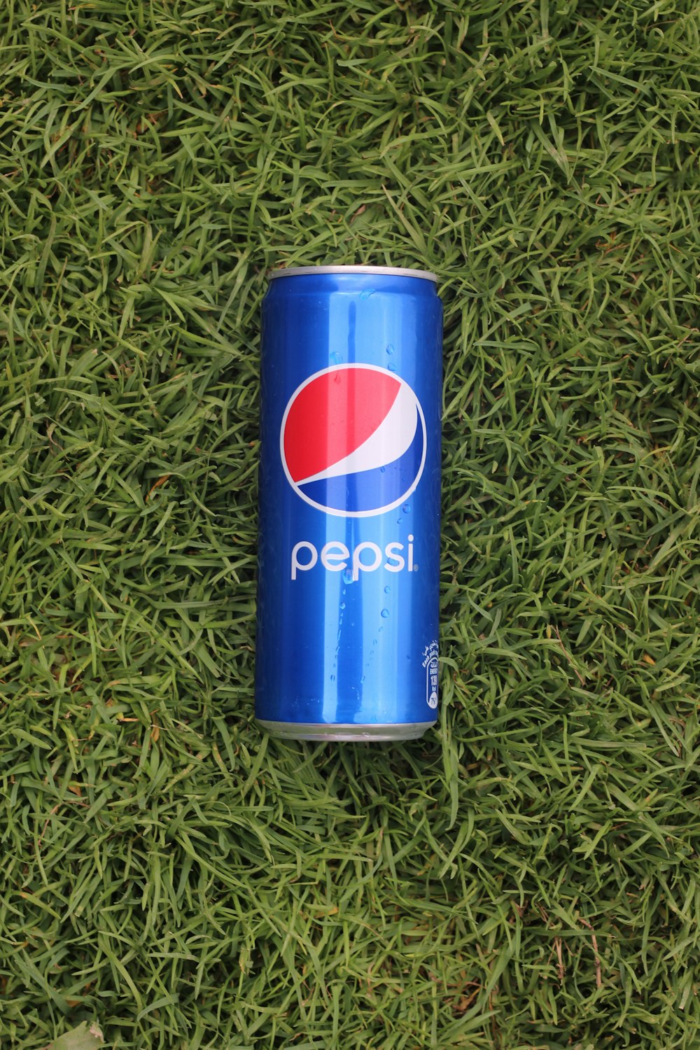 a can of pepsi sitting on top of a lush green field