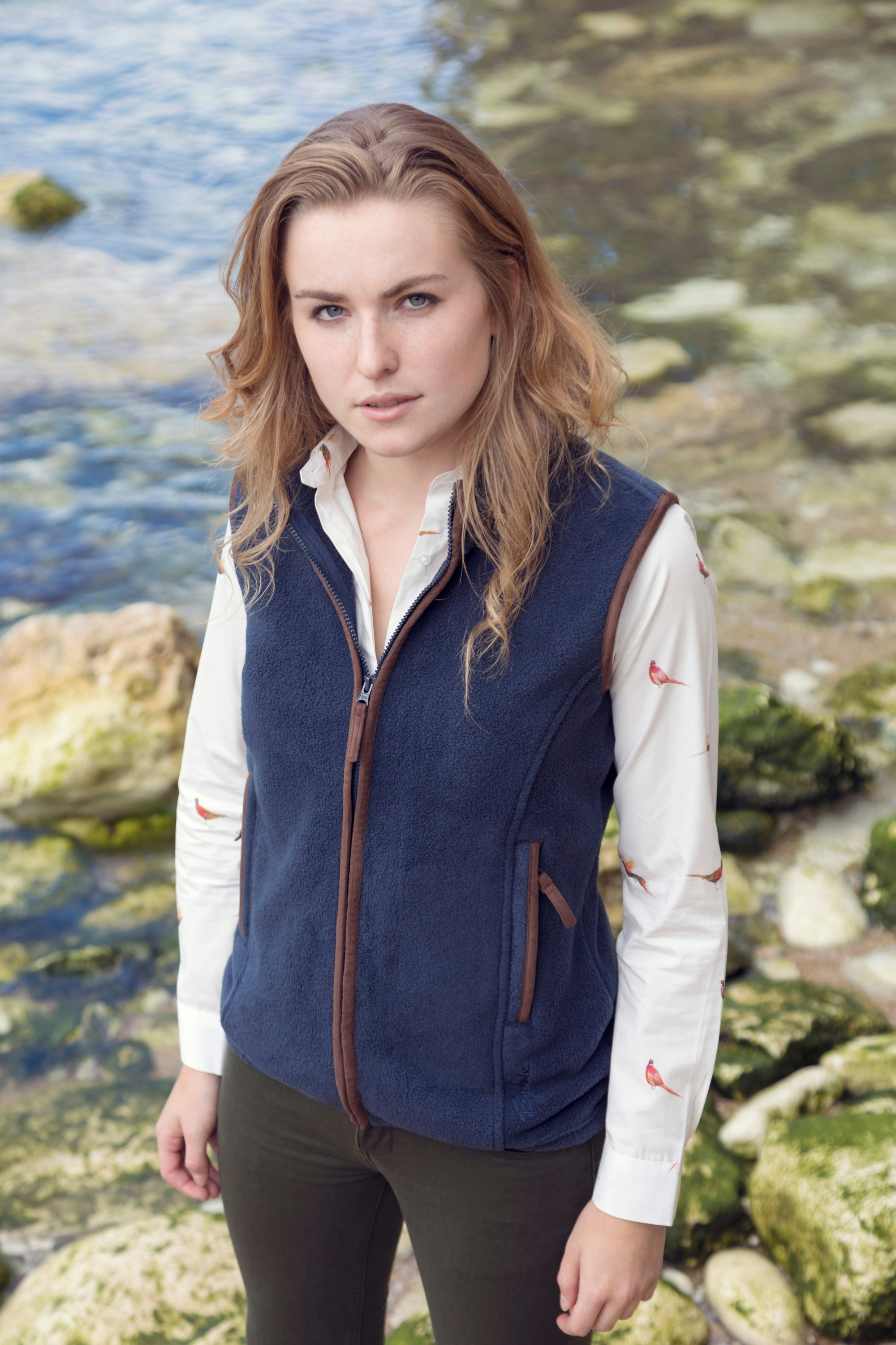 a woman in a blue vest standing by a body of water