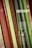 Vertical, glossy panels of alternating colors, primarily in shades of red, green, and dark tones. The panels are aligned closely, creating a pattern of contrasts between the colors and reflections. The background is slightly blurred, hinting at an indoor setting.