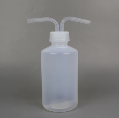 A semi-transparent plastic wash bottle with two bent dispensing nozzles. The bottle has a cylindrical shape with a white cap, and the background is a plain, neutral grey.