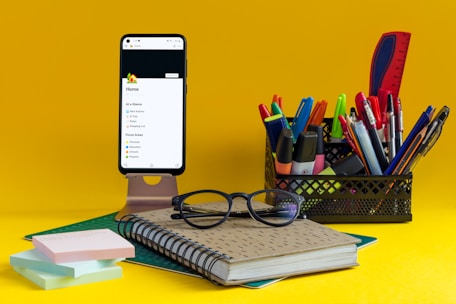 a notebook, pen, glasses and cell phone on a yellow background
