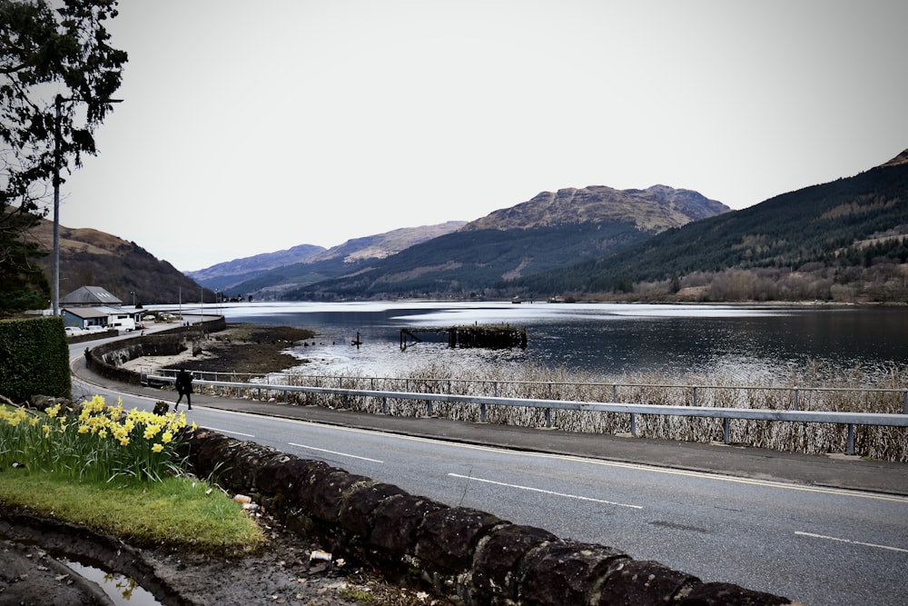 a person walking on the side of a road next to a body of water