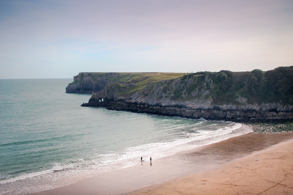 two people walking on a beach near the ocean