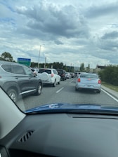 Sparse traffic is seen on a multi-lane road surrounded by greenery and illuminated traffic lights under a cloudy sky.