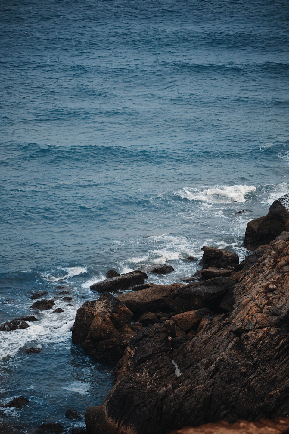 Rocky coastline with choppy blue ocean stretching into distance, surrounded by large jagged rocks