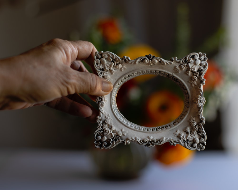 a person holding a picture frame in front of a vase