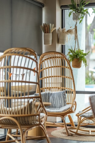 A cozy living room featuring bamboo and rattan furniture with soft beige cushions, surrounded by lush green plants and warm natural light.