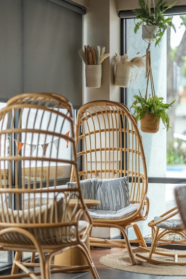 A sunlit living room corner with woven rattan chairs, soft linen cushions, and a terracotta pot holding a lush green plant.