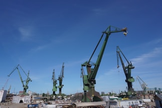 Close-up of precision metalwork with a maritime shipyard in the background under clear skies.