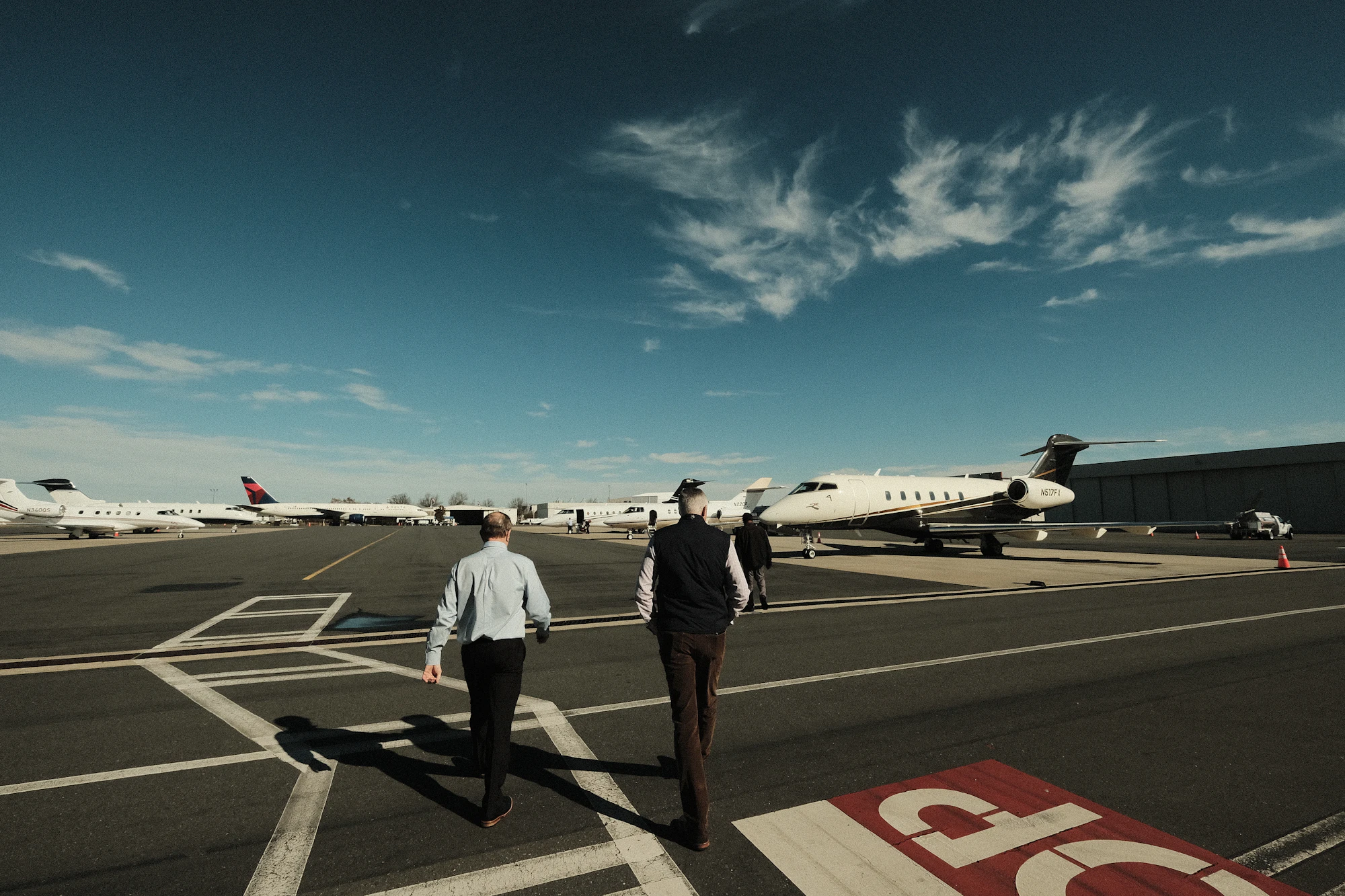 Two crew members walking across the apron towards parked private jets, the operator side of the charter broker vs operator question