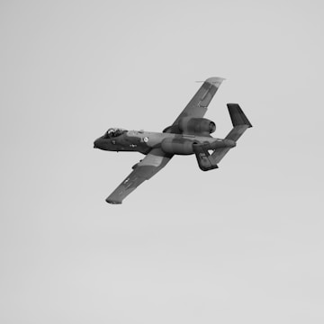 A military aircraft is flying at an angle against a clear sky. The aircraft has distinct engines located on either side of the fuselage and a heavily armored body.